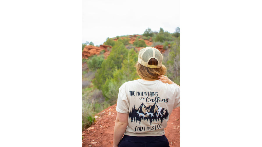 Shirt — The Mountains Are Calling design on a cream tee, red rock trail behind